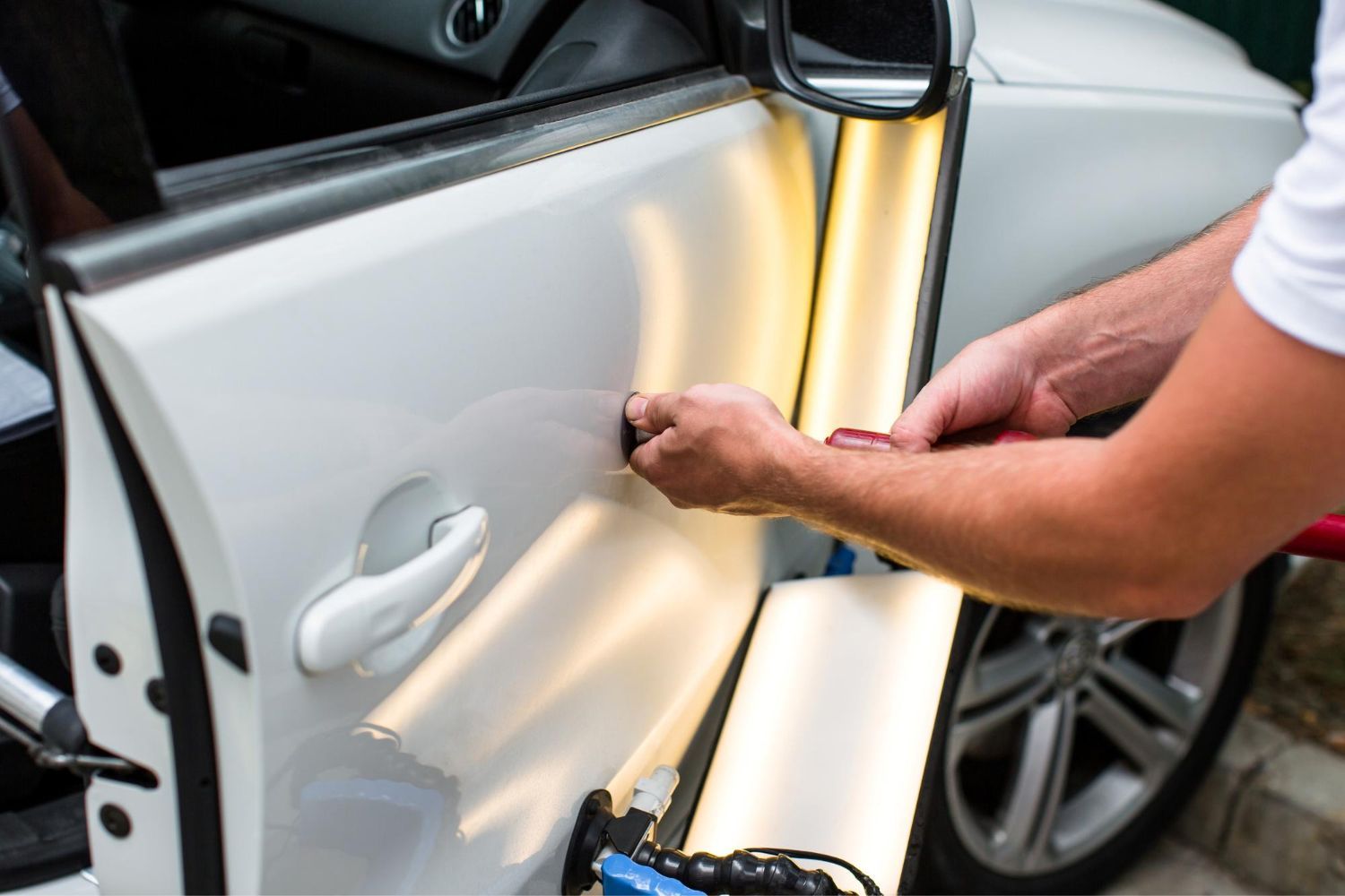 Person removing car door dent with a repair tool on a white vehicle