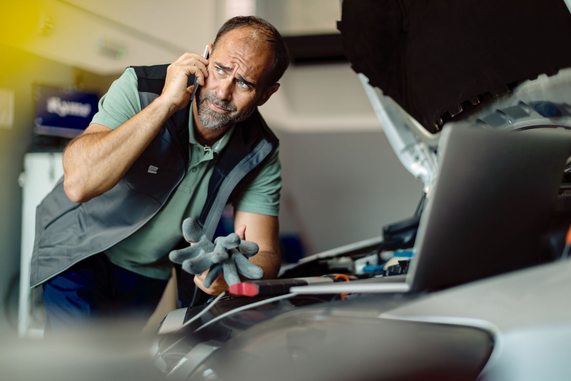 A man is talking on a cell phone while working on a car.