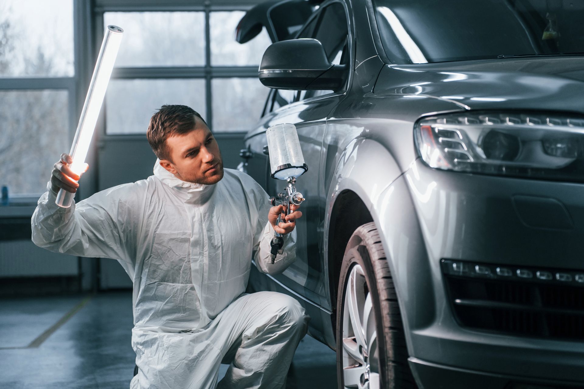 A man is painting a car in a garage while holding a light.