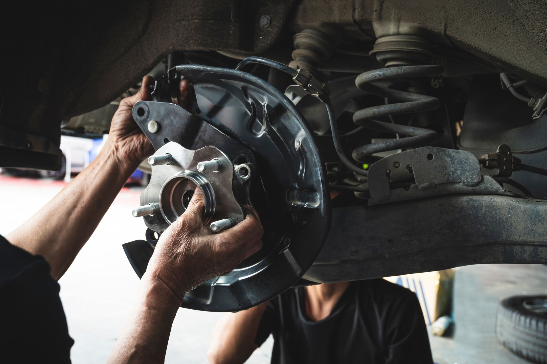 Hands installing a car brake rotor in an auto repair shop.