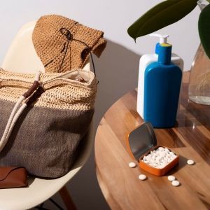 Un sac en paille, un chapeau, des flacons-pompes et une boîte de pilules blanches ouverte reposent sur une table en bois