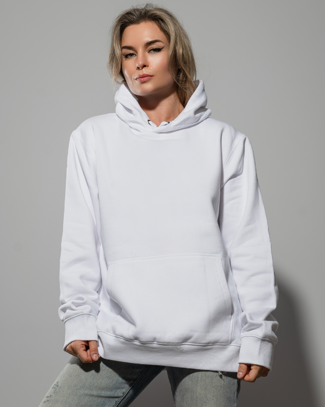 Une personne posant en sweat-shirt à capuche blanc uni sur fond gris uni.