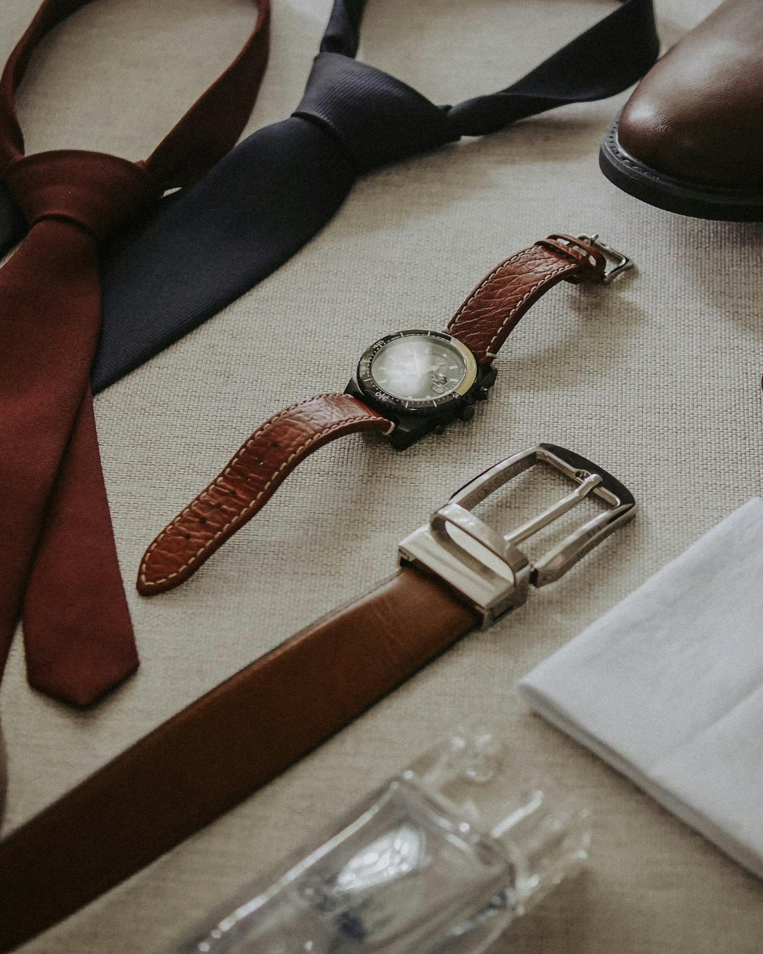 Accessoires de cérémonie pour homme comprenant une montre marron, deux cravates, une ceinture en cuir.