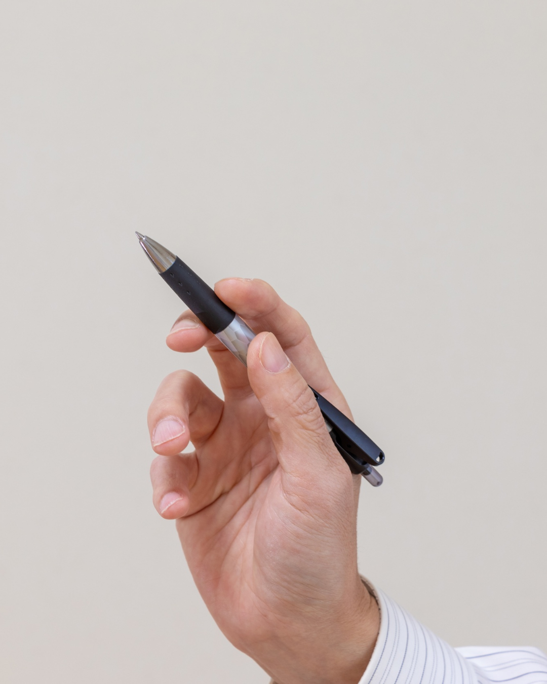 Une main tient un stylo rétractable noir et argent sur un fond clair et uni.