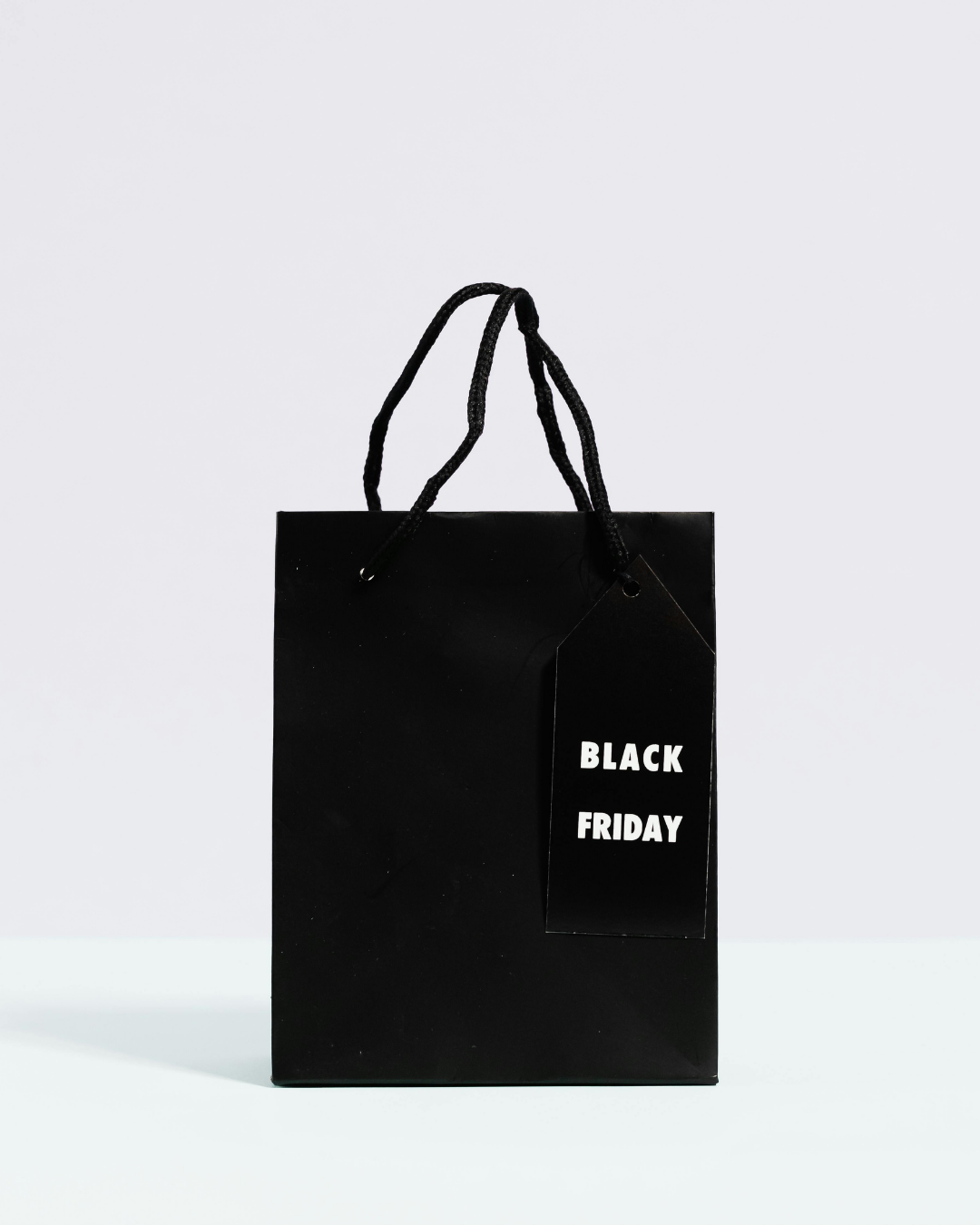 Un sac cadeau noir avec des poignées et une étiquette sur laquelle on peut lire « BLACK FRIDAY » en lettres blanches