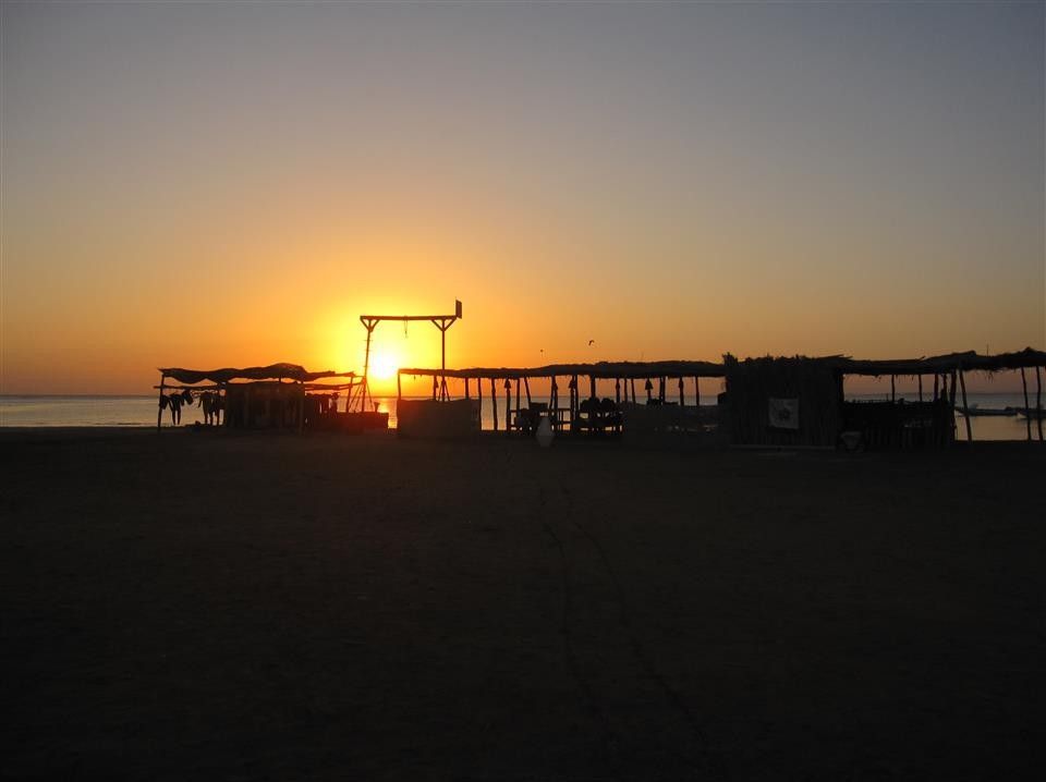 Een zonsondergang boven een strand met een paar gebouwen op de voorgrond