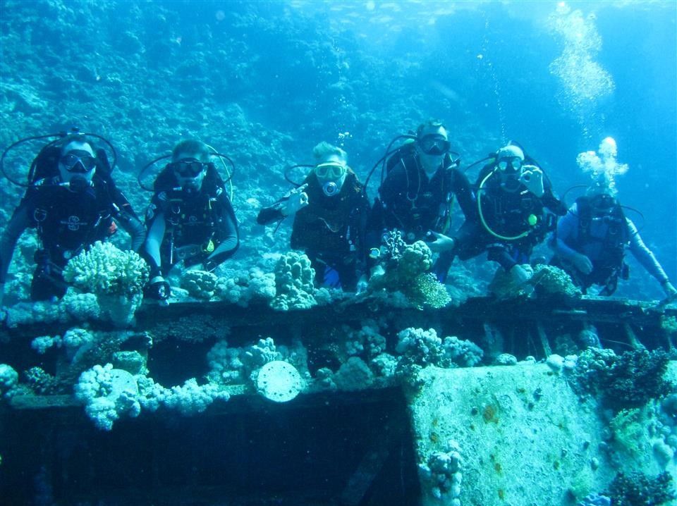 Een groep duikers staat bovenop een scheepswrak in de oceaan.