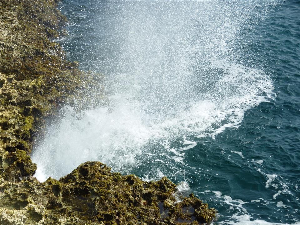 Een grote golf beukt tegen een rotsachtige kustlijn