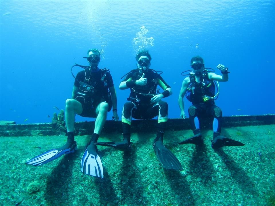 Drie duikers zitten op een rots in de oceaan.