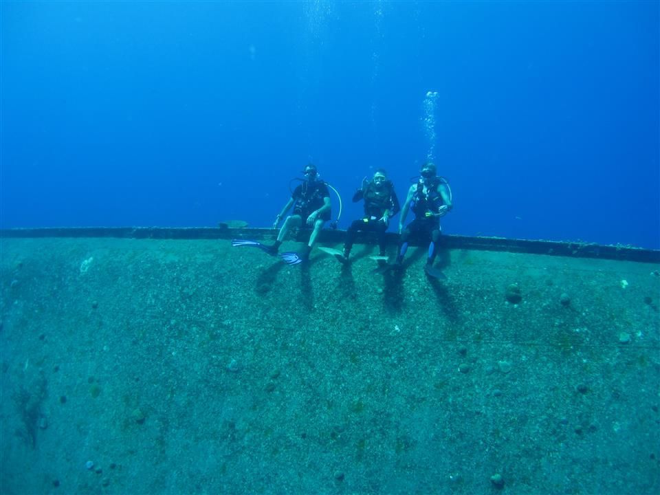 Drie duikers zitten bovenop een grote rots in de oceaan.