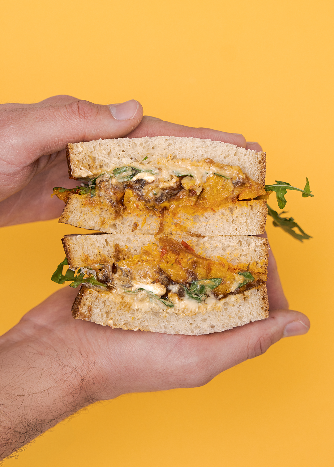 Hands holding the Messalina sandwich on a mustard yellow background 