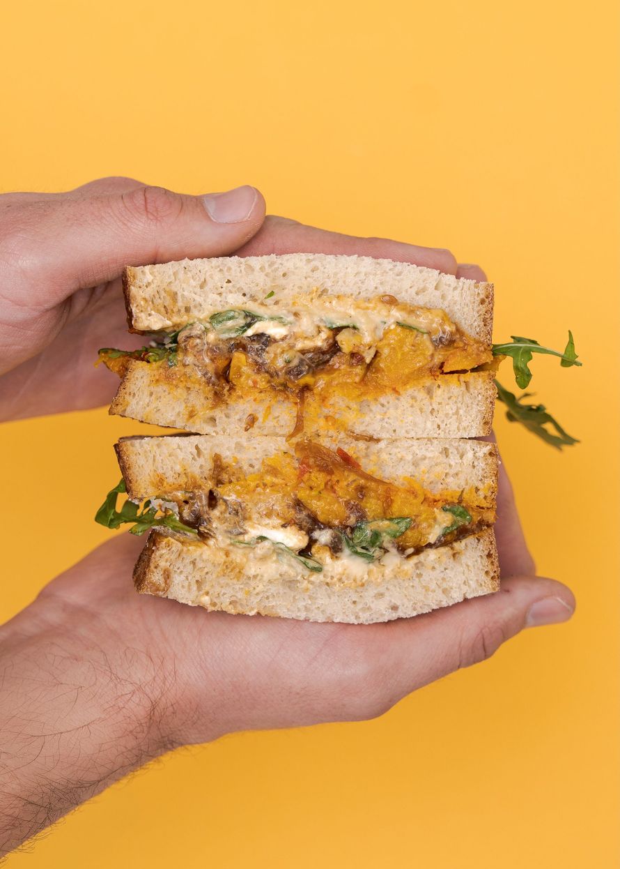 Hands holding the Messalina Sandwich on a mustard yellow background 