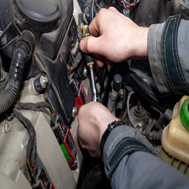 A mobile mechanic is working on a car engine with a wrench.