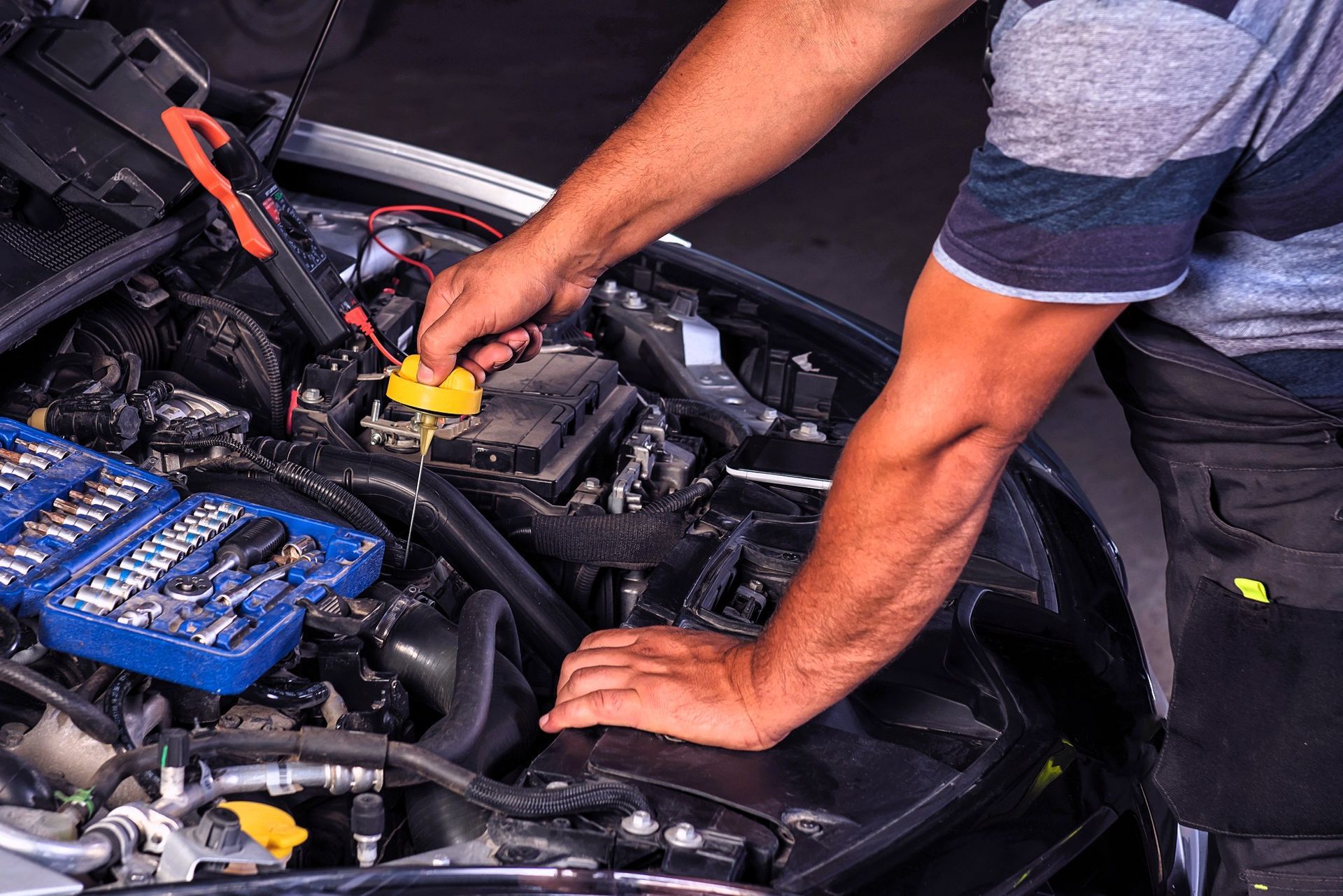 Person checking car engine oil level with dipstick near an open tool kit