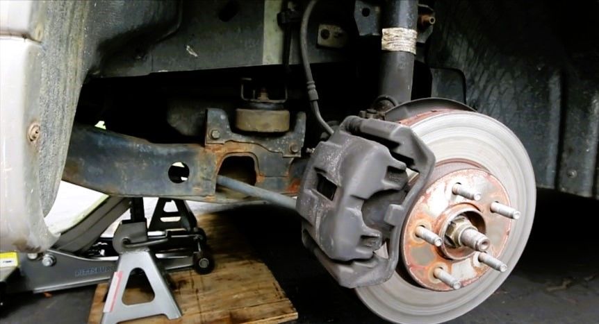 Vehicle wheel hub and brake assembly exposed with a jack and jack stand for maintenance