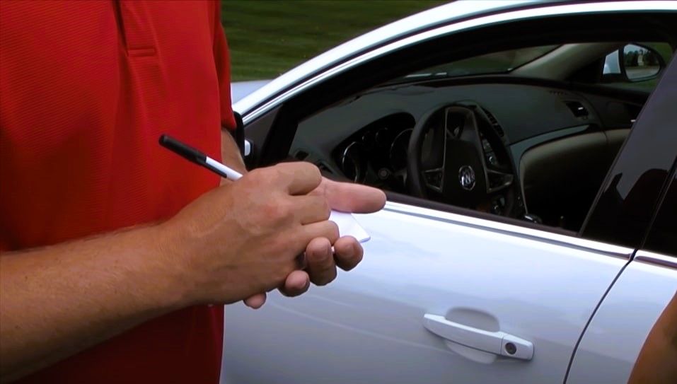 Man taking notes at car accident scene for insurance report.