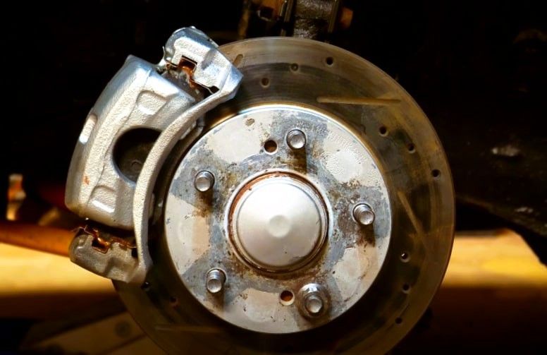 Close-up of a car's brake system with a metallic caliper and rusted brake disc.