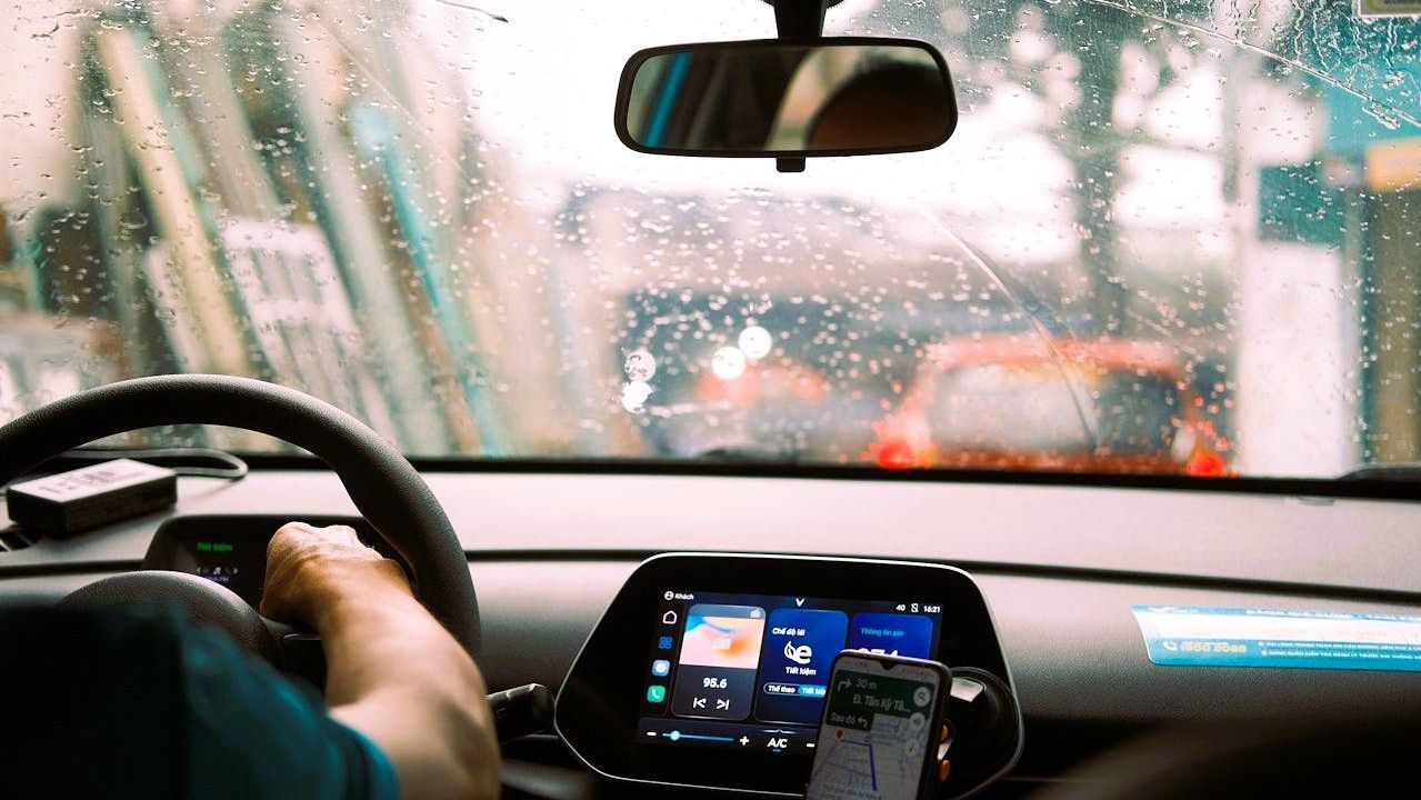 Driver's view from inside a car in the rain, with focus on the wet windshield and dashboard.