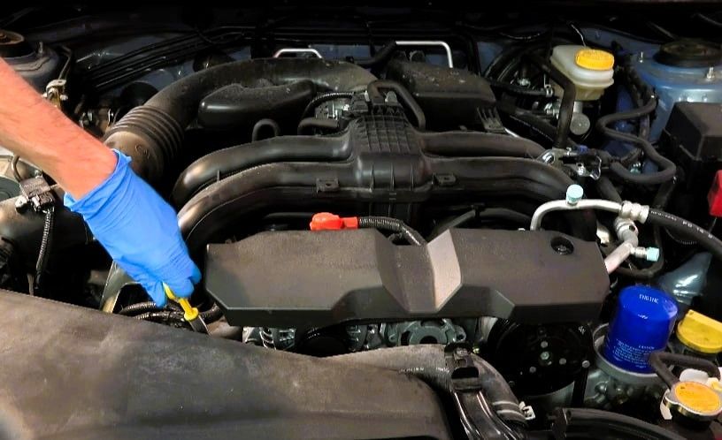 Mechanic in blue gloves checking car engine with yellow dipstick