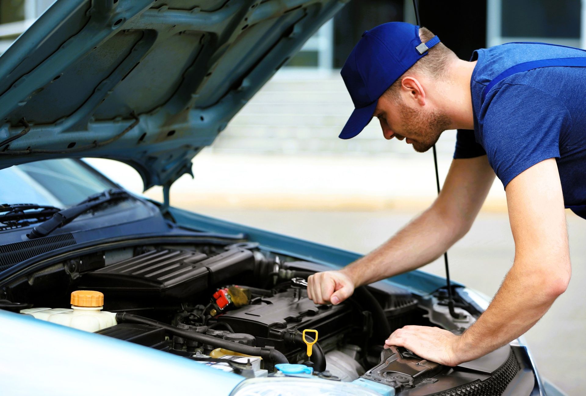 A mobile mechanic in a blue shirt and cap working on a car engine