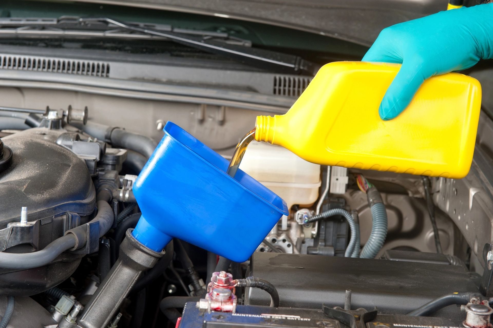 Gloved hand pouring oil into funnel during car oil change maintenance