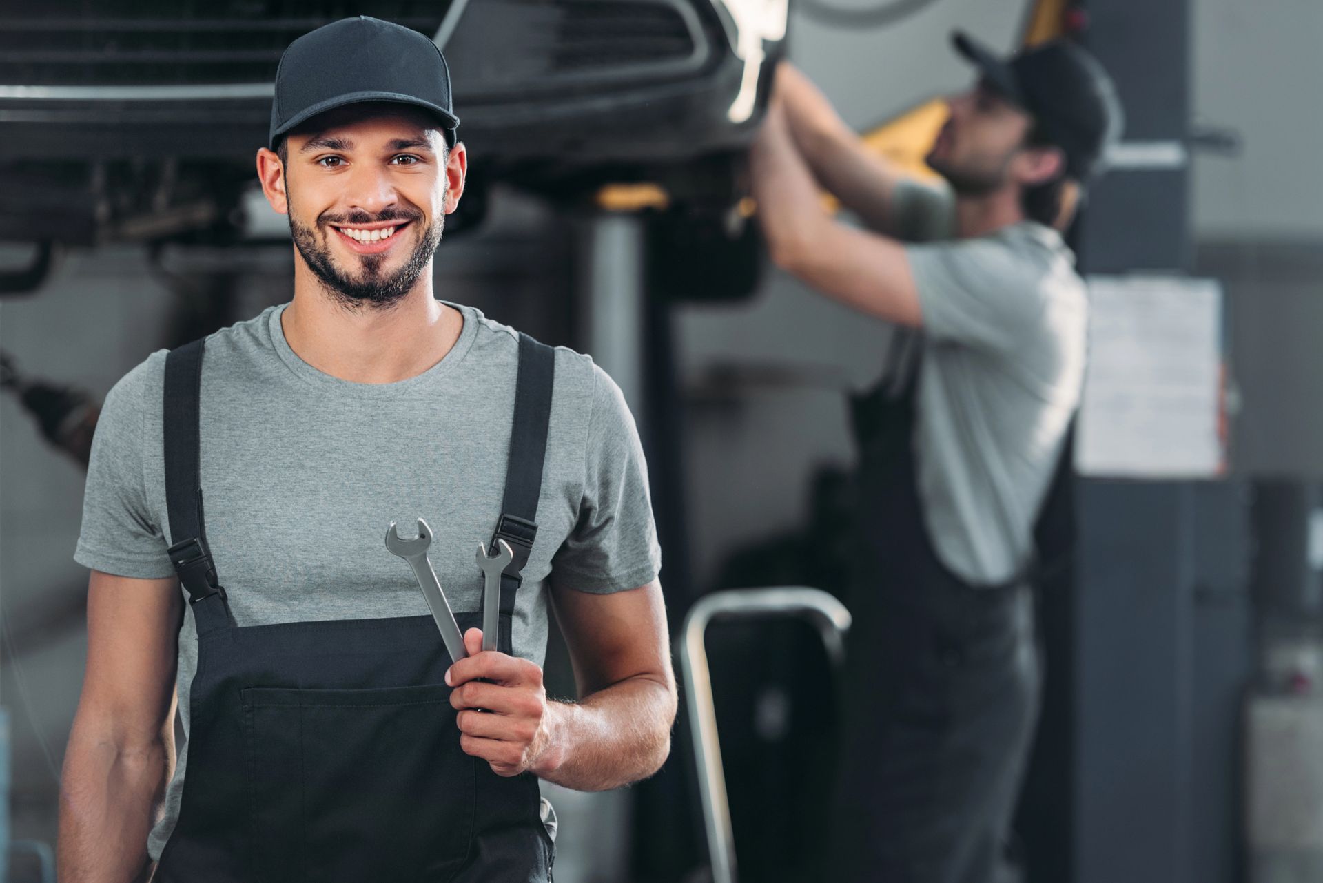 Mechanic holding wrenches with colleague working on car overhead in garage