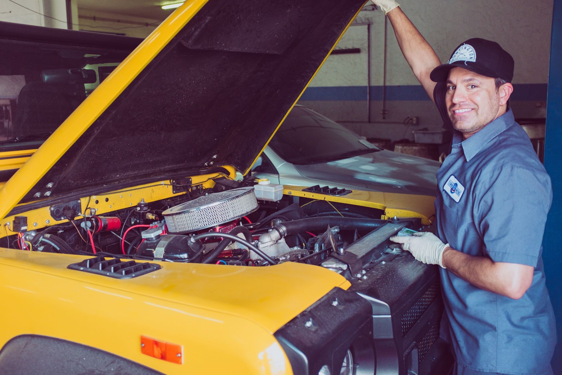 A mechanic is working on a yellow car in a garage.