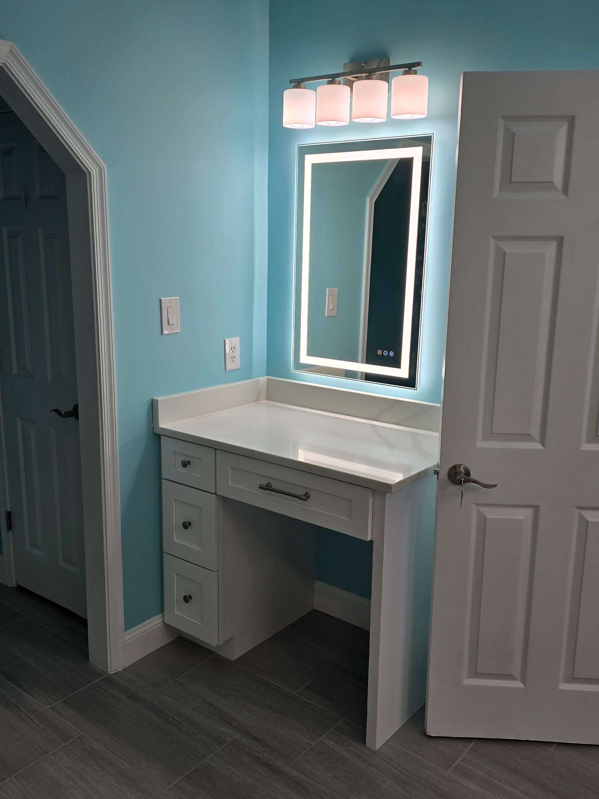 Vanity area with a white desk, lighted mirror, and turquoise walls.