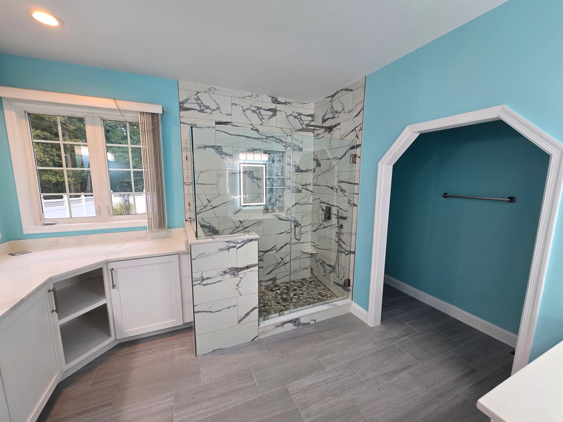 Bathroom with blue walls, white cabinets, marble shower, and gray tile floor.