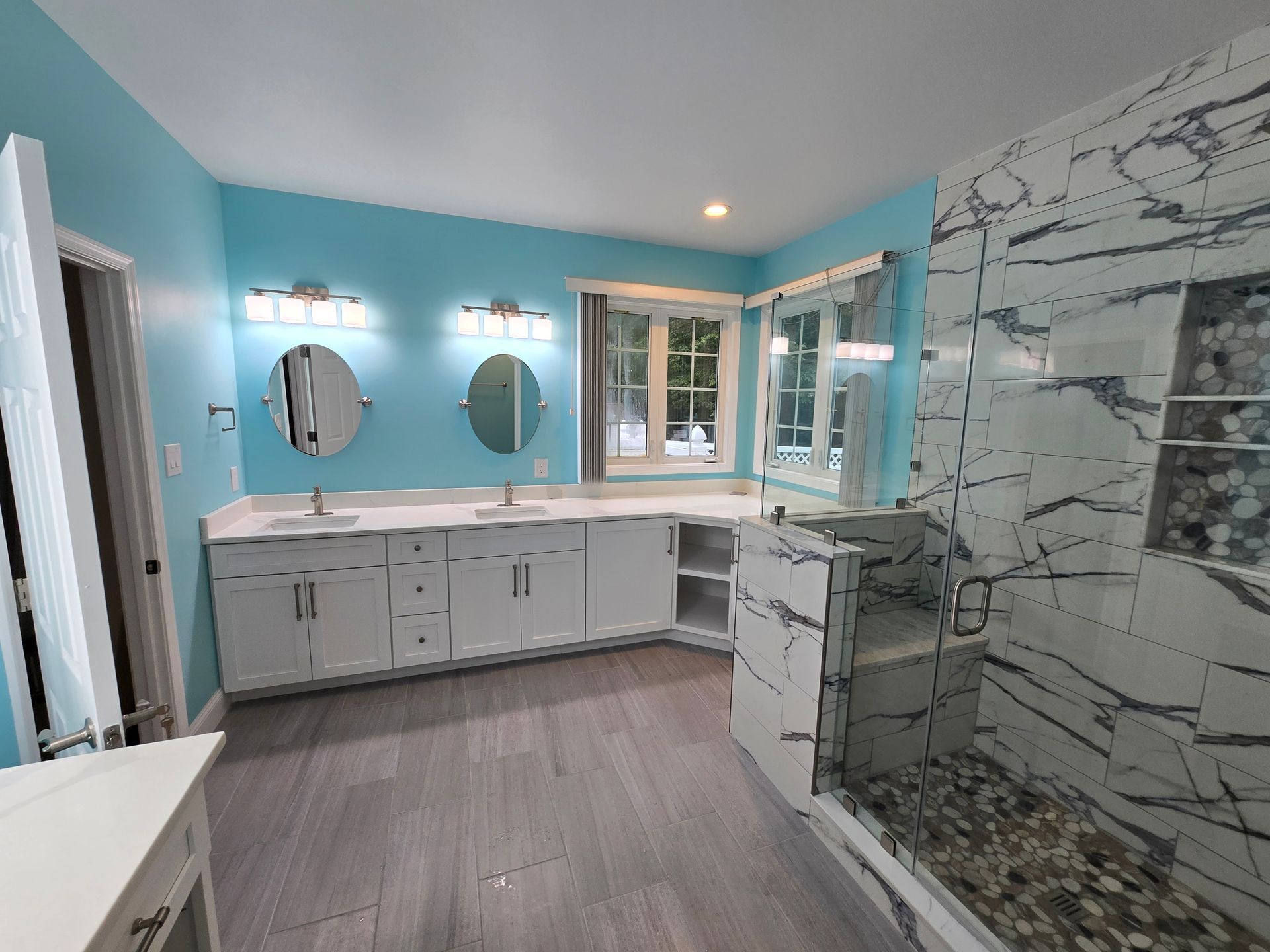 Modern bathroom with blue walls, white vanity, gray floor, and marble shower.