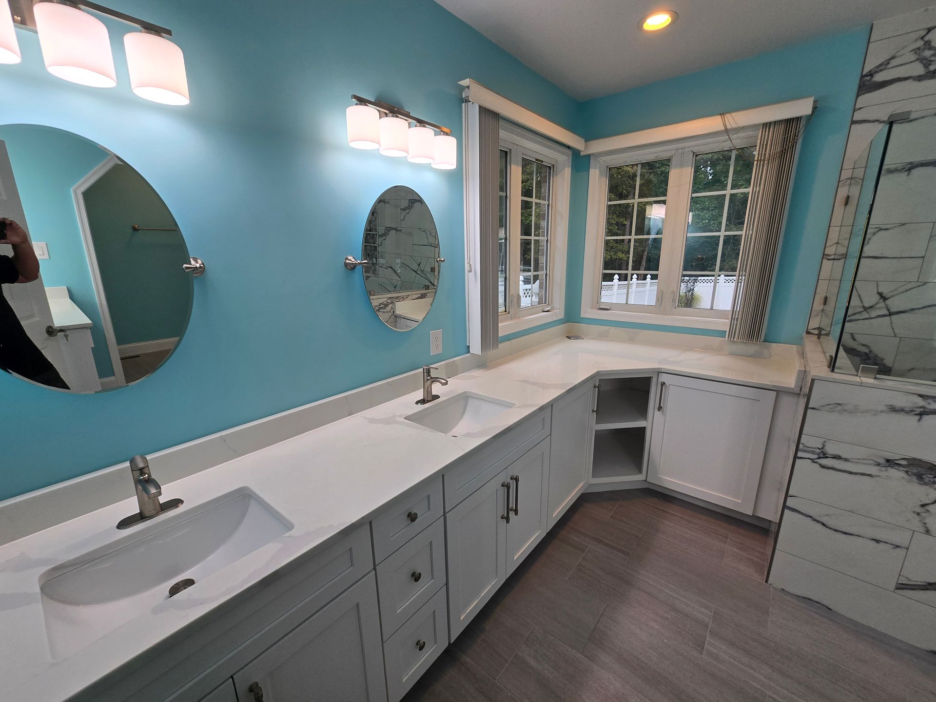 Bathroom with light blue walls, white cabinets, two sinks, and a window.
