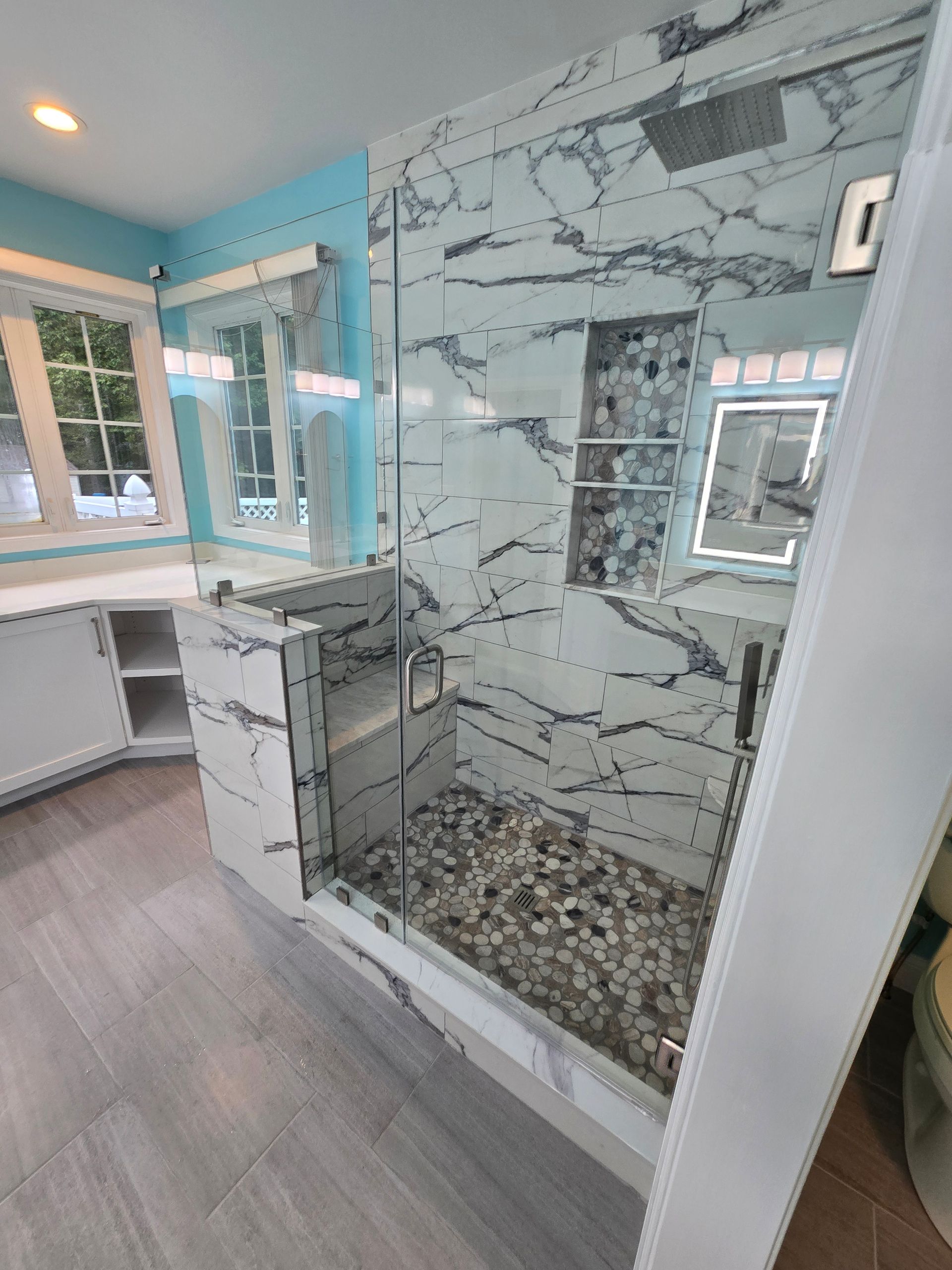 Modern bathroom with marble shower, pebble floor, glass door, and blue walls.