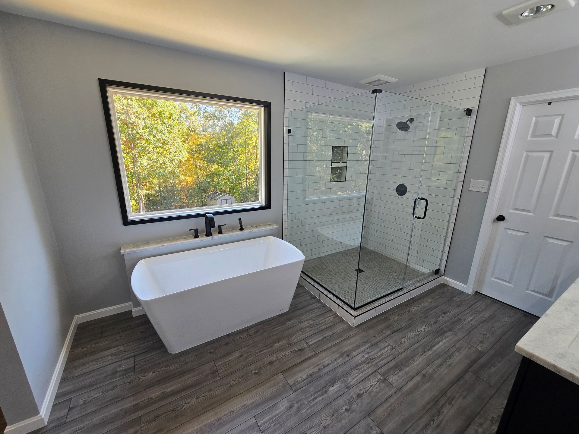 Modern bathroom with a white freestanding tub, glass shower, and gray wood-look floor.