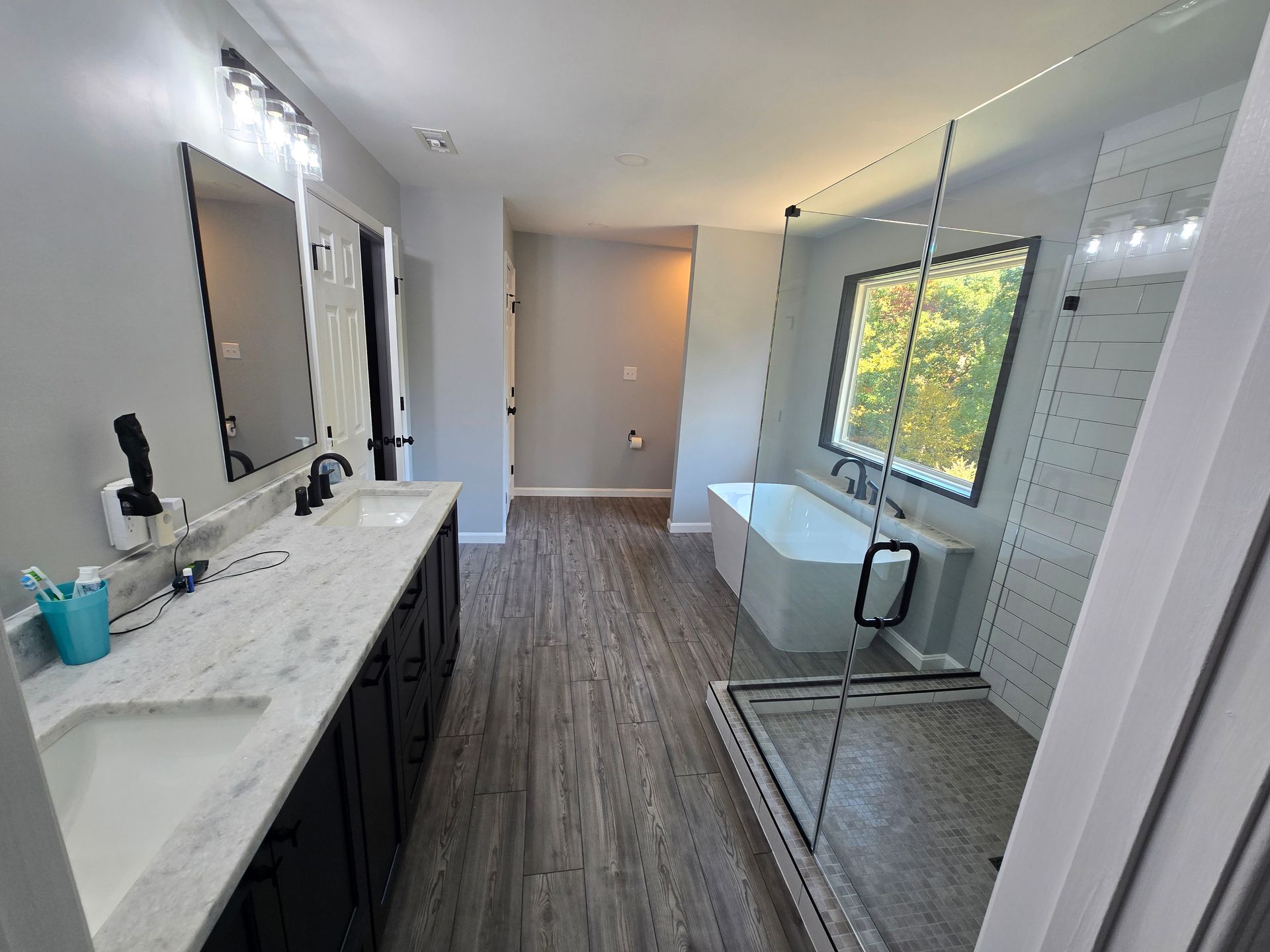 Modern bathroom with dual sinks, a tub, and a glass shower. Gray walls and wood-look flooring.