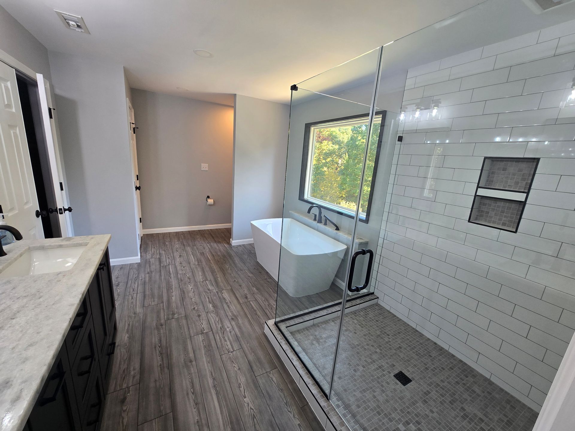 Modern bathroom with a white tub, shower, and vanity. Gray walls and flooring.