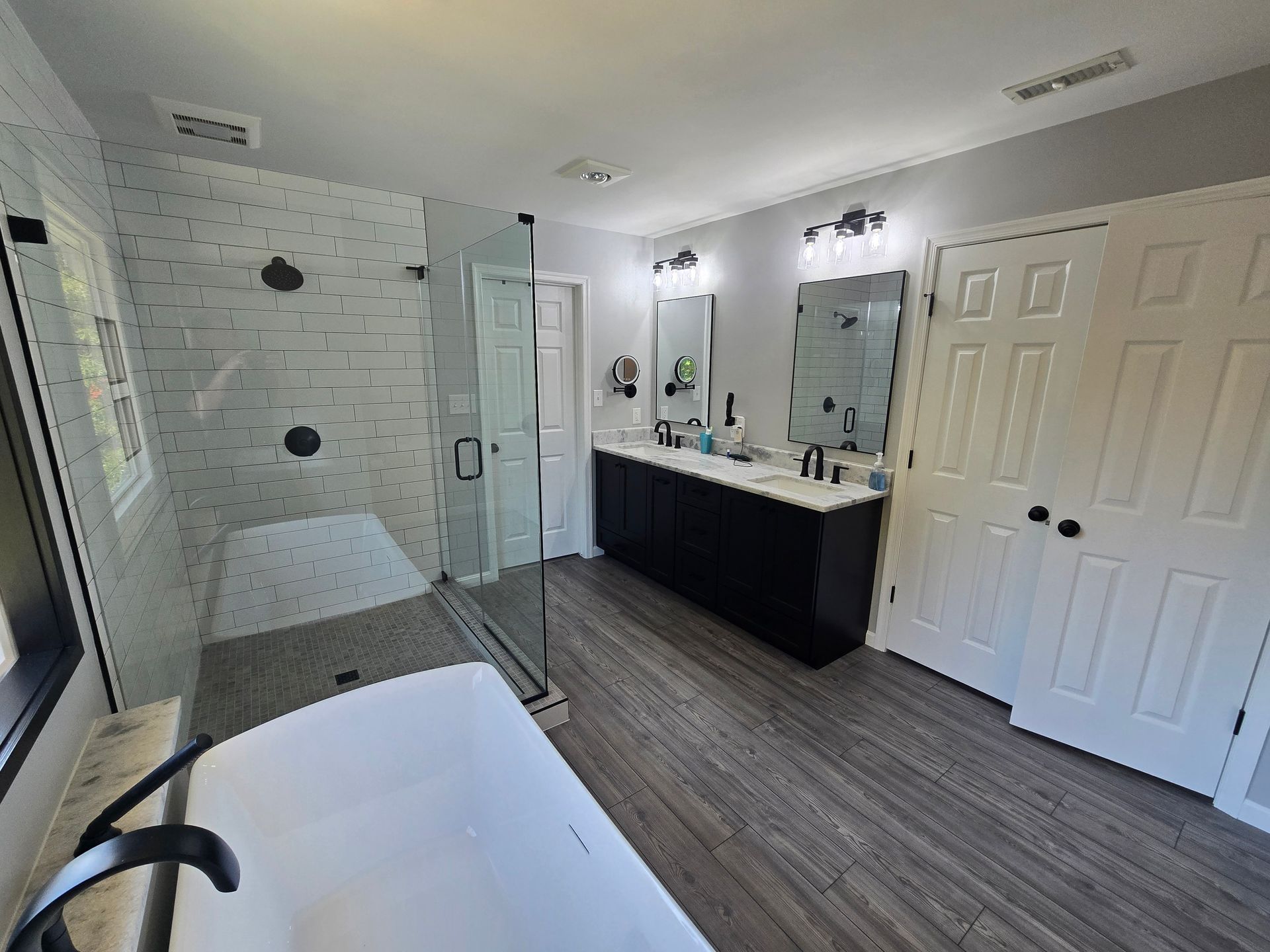 Modern bathroom with a bathtub, shower, double vanity, and wood-look flooring. White and black accents.