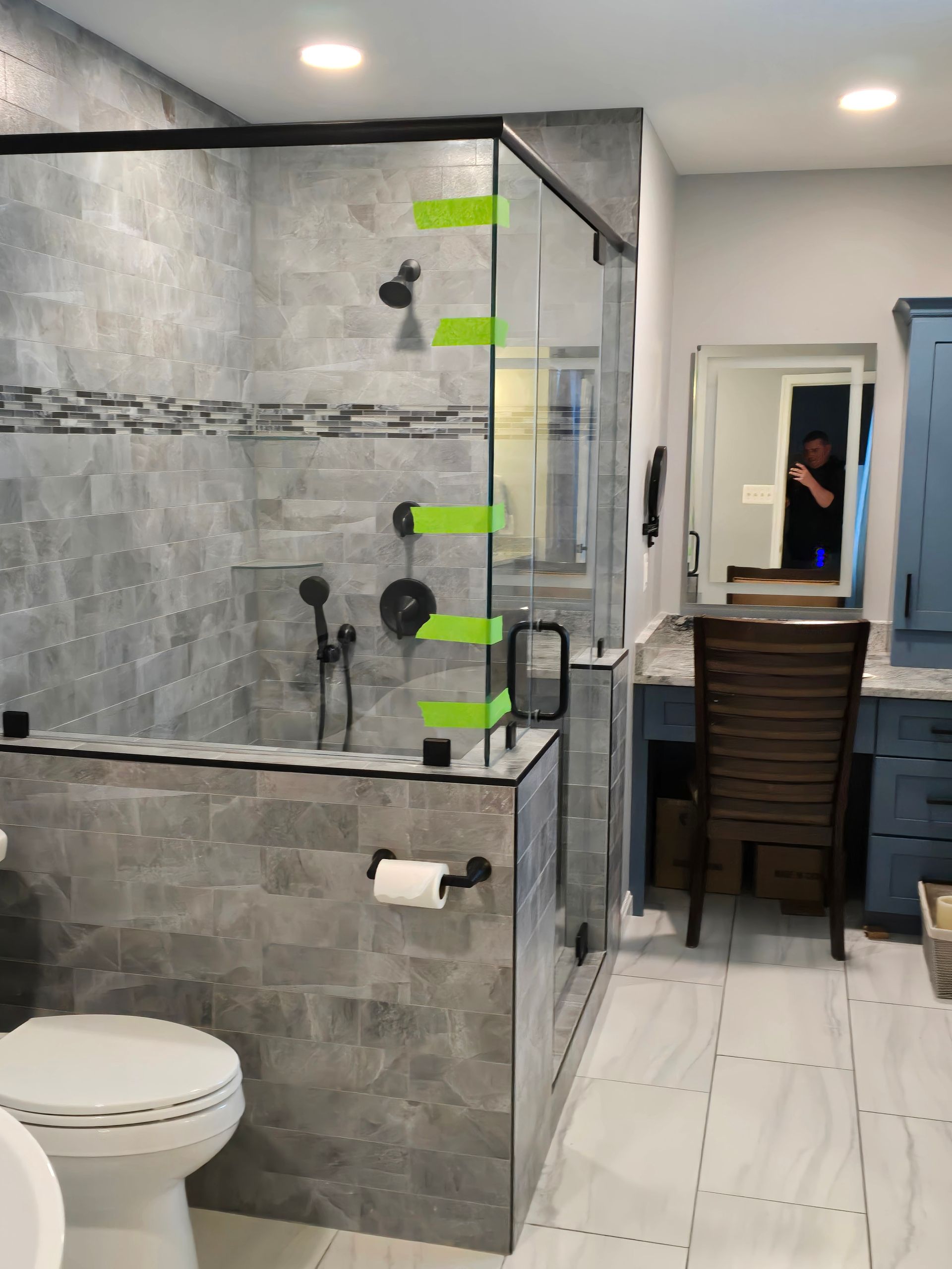 Modern bathroom with a tiled shower, glass door, toilet, and vanity with blue cabinets.