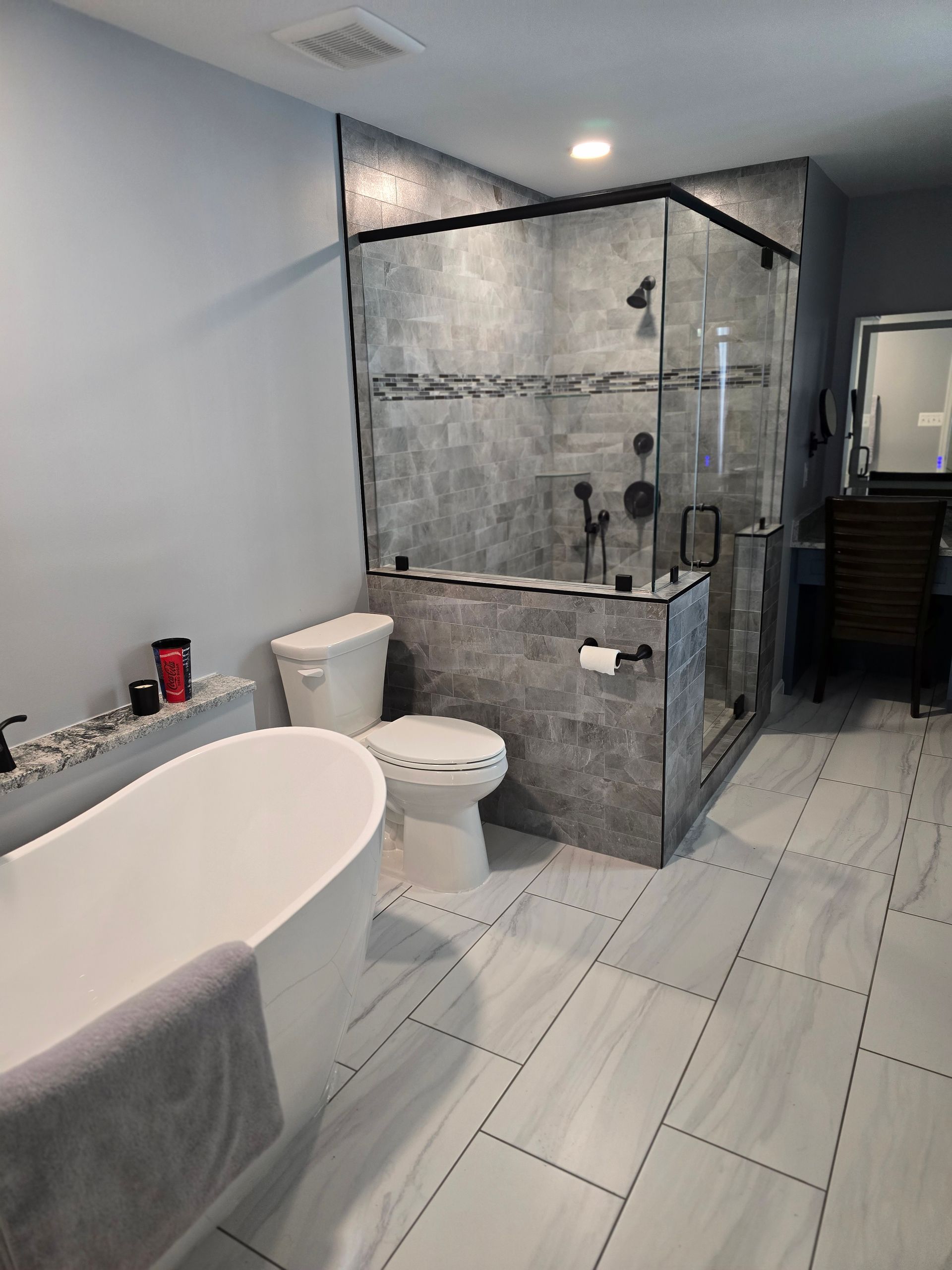 Modern bathroom with a white tub, toilet, gray tile shower, and light blue walls.