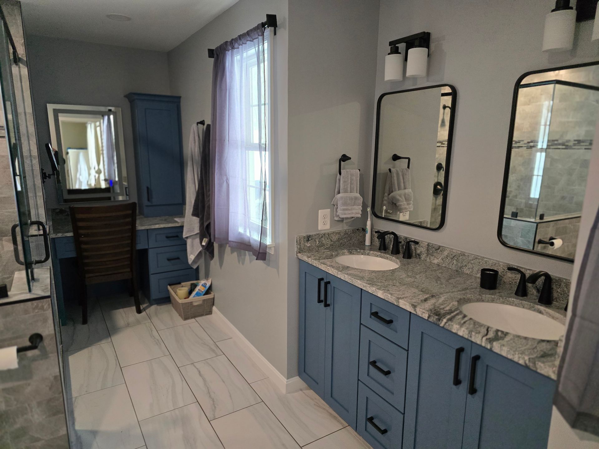 Blue bathroom with double vanity, two mirrors, and a window.