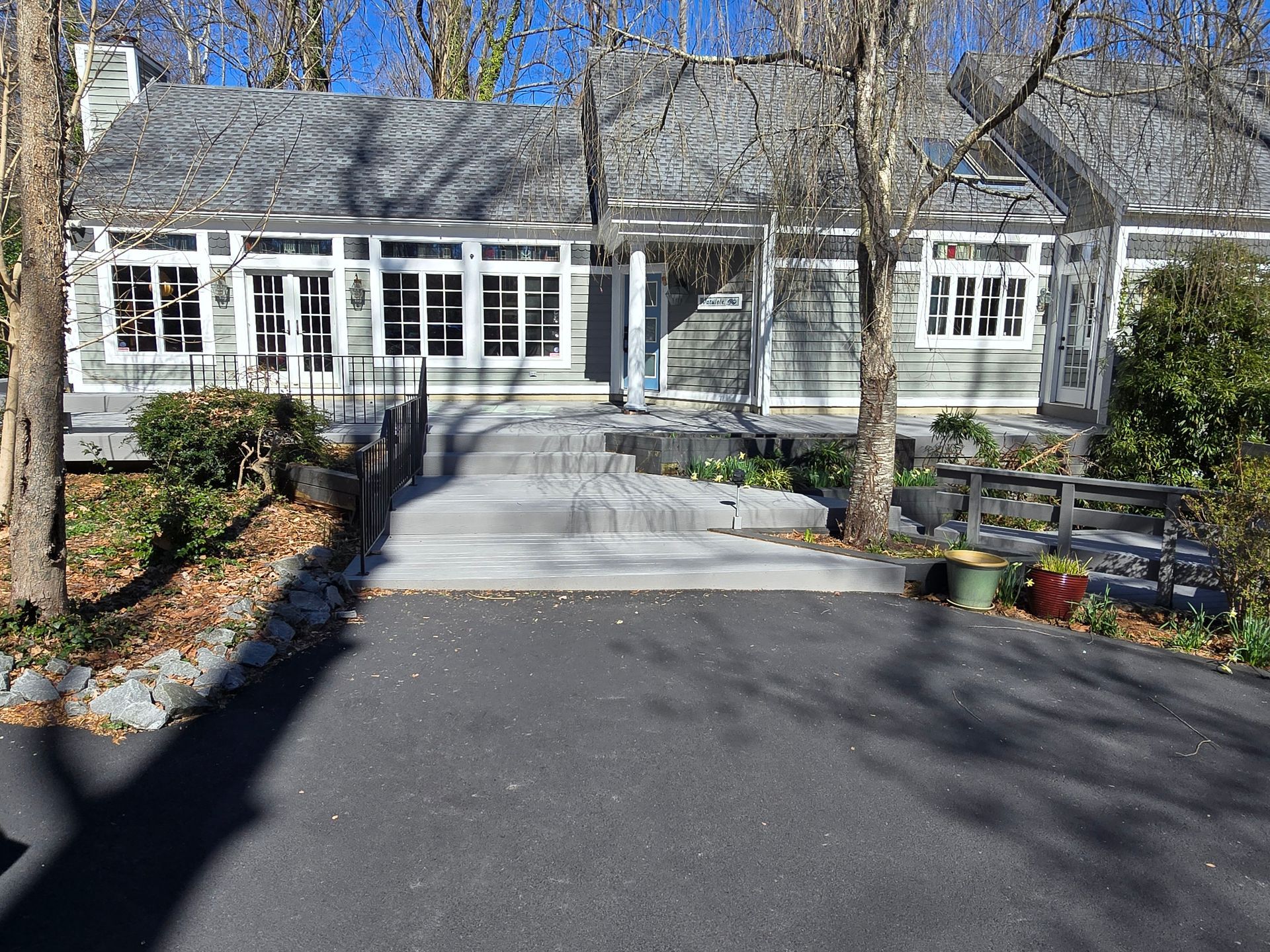 Gray house with a paved driveway and concrete steps leading to the entrance. Trees flank the building.