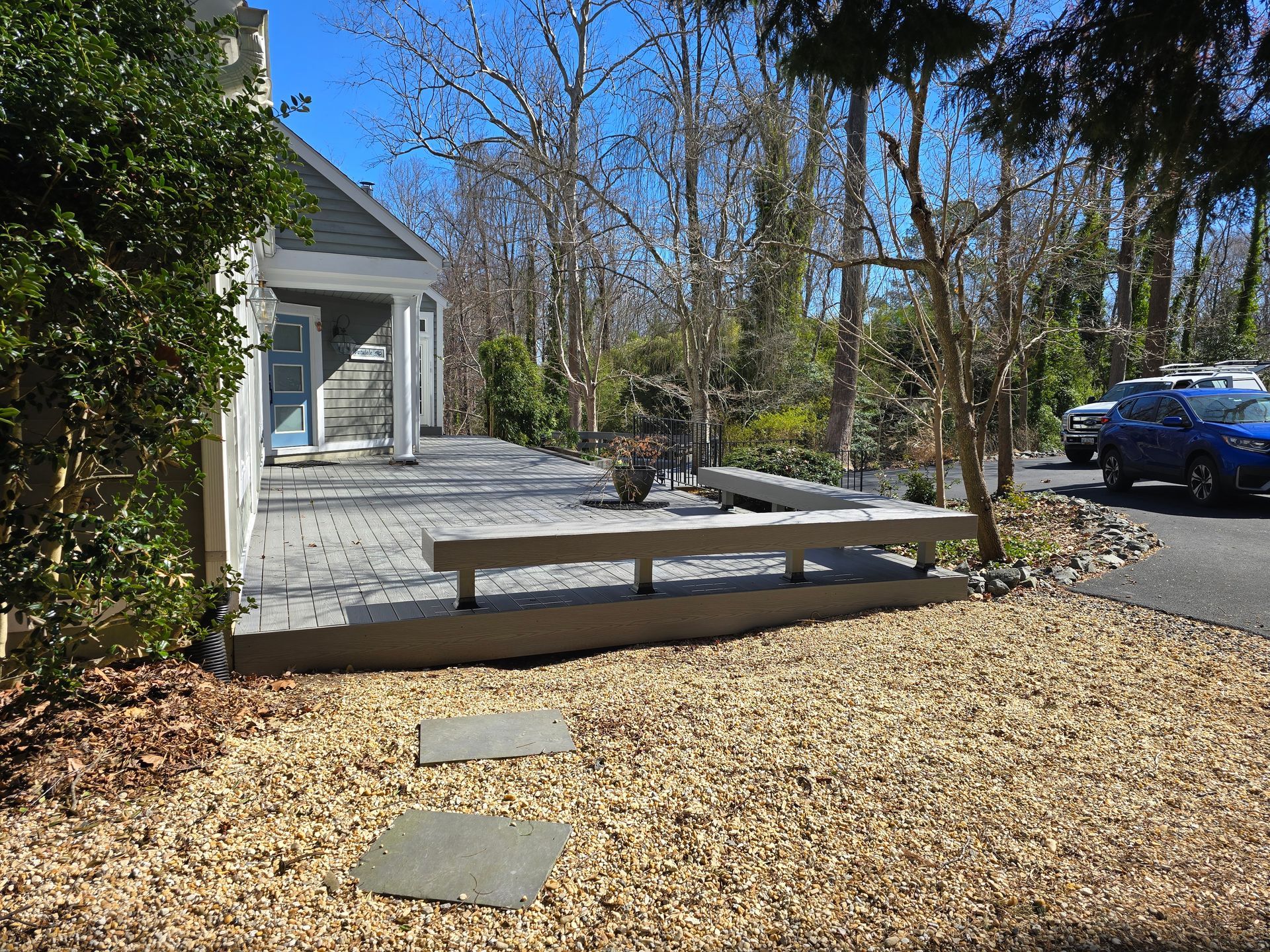 Exterior view of a home with a paved patio, stone bench, and gravel landscaping. Blue car parked on the driveway.