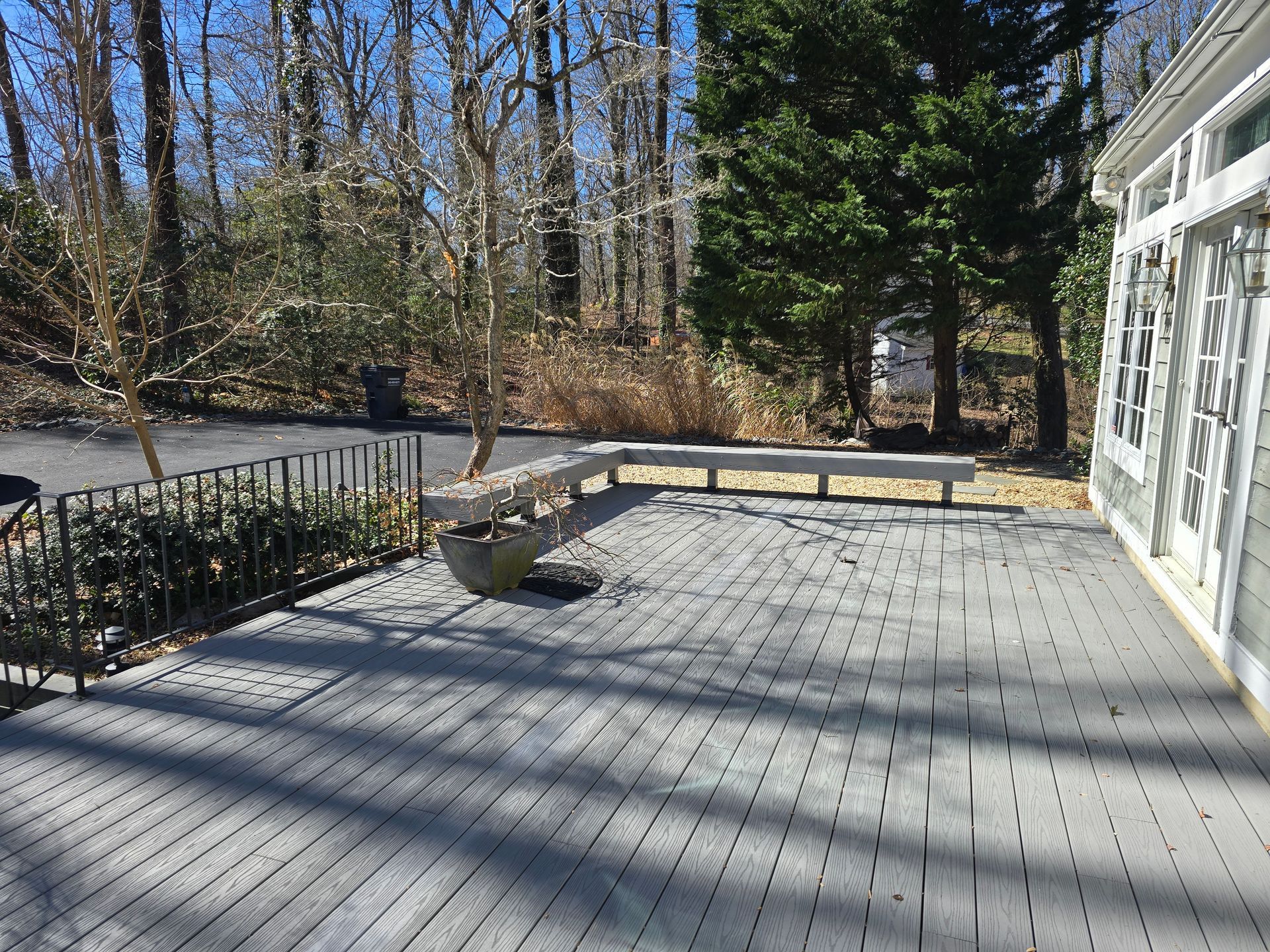 Gray wooden deck with built-in benches, a metal railing, and a view of trees and a house.