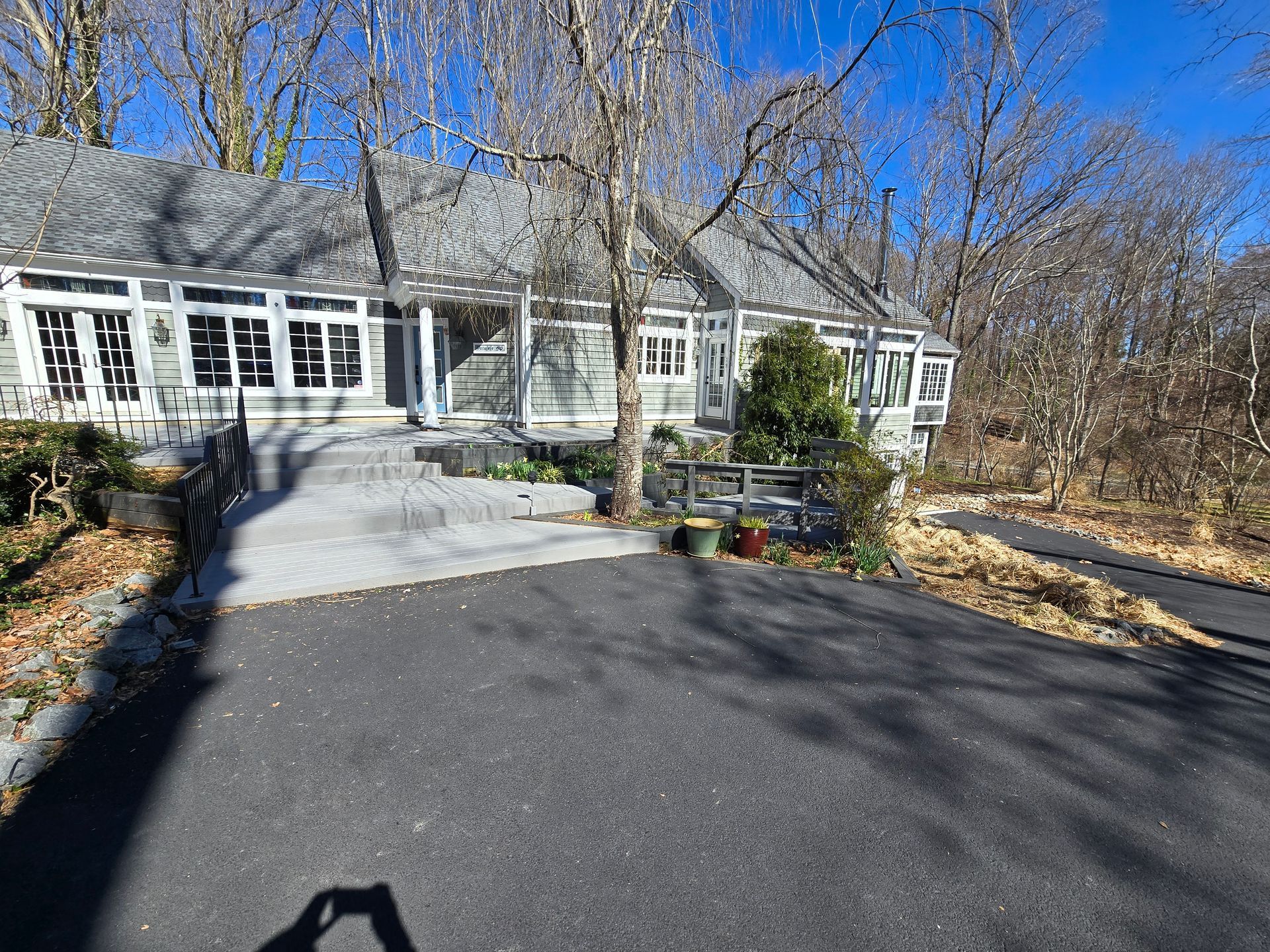 Gray house with a dark driveway, trees, and blue sky.