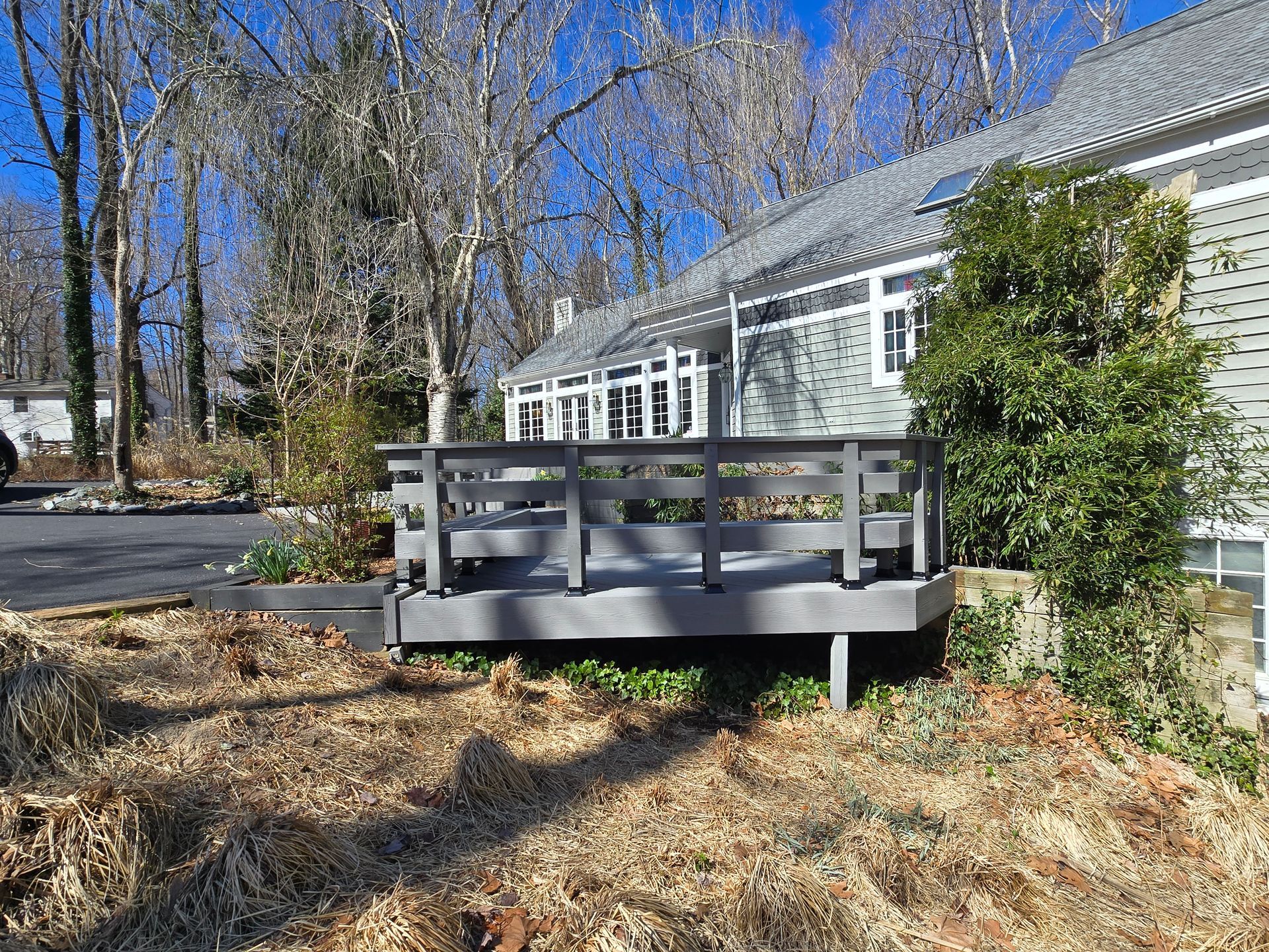 Gray deck attached to a gray house, set in a yard with dry grass and trees.