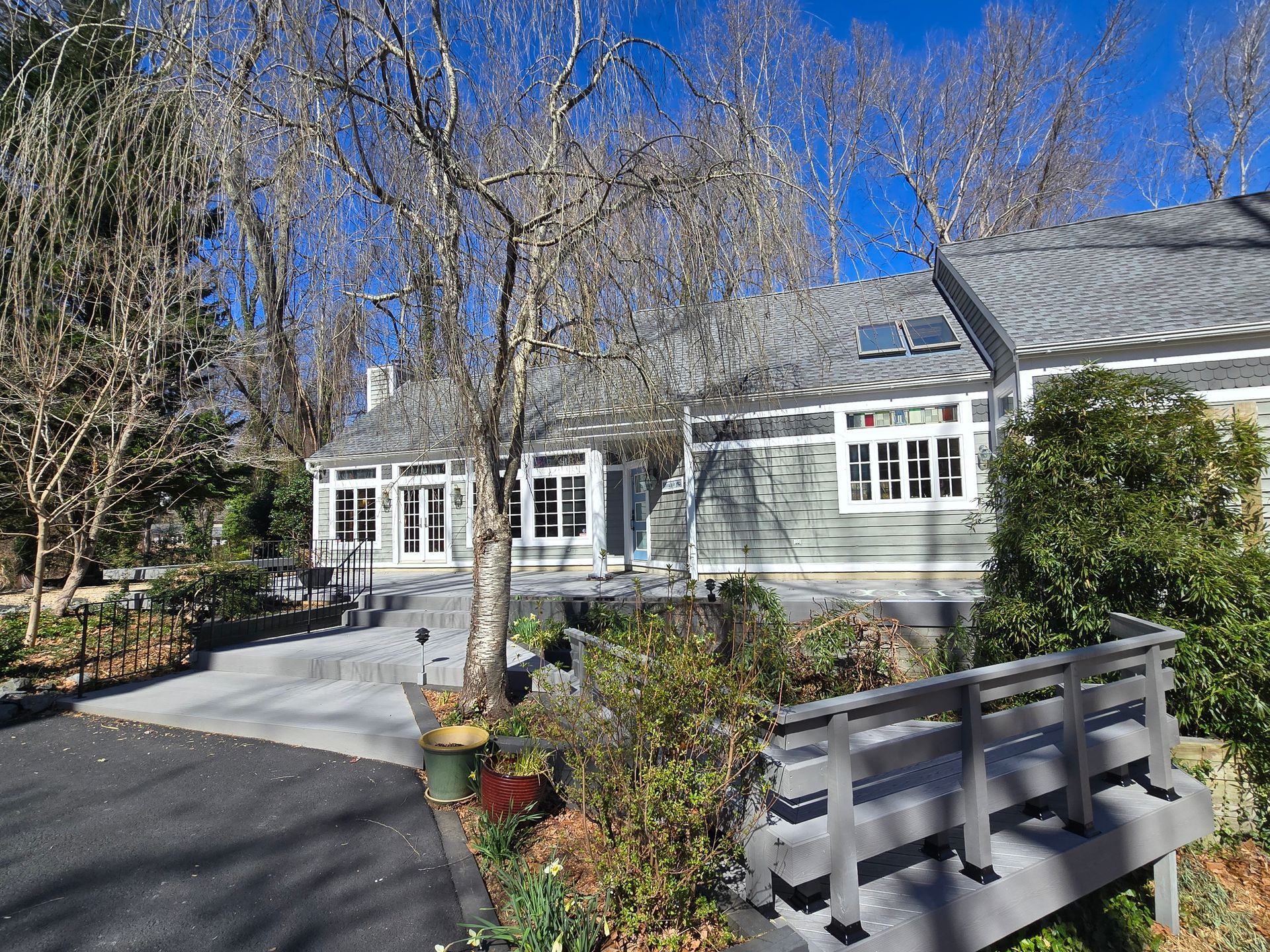 House with gray siding and roof, front porch, and walkway, trees, and blue sky.