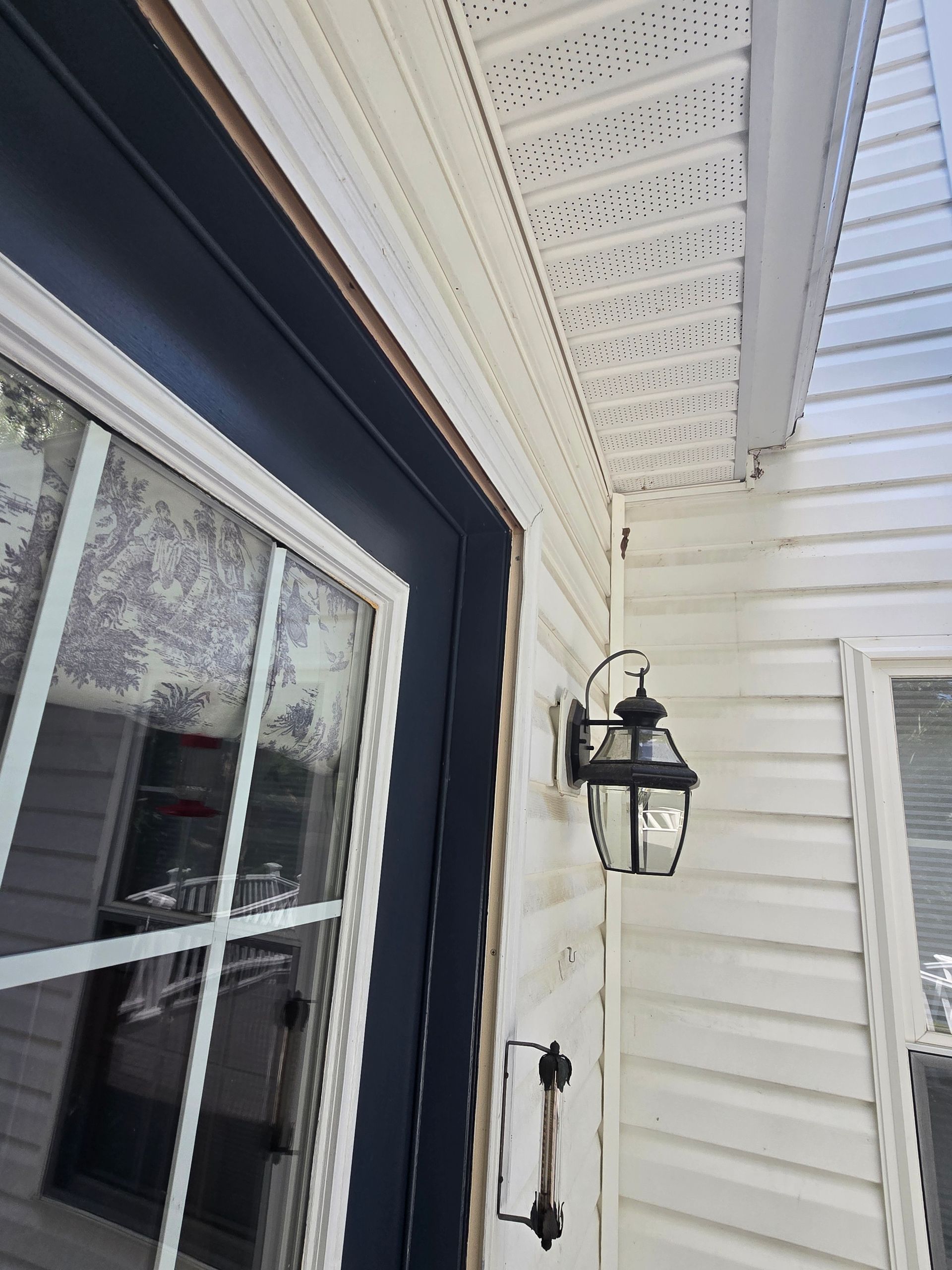 White siding on a house with a black door frame, a window, and a wall-mounted light fixture.