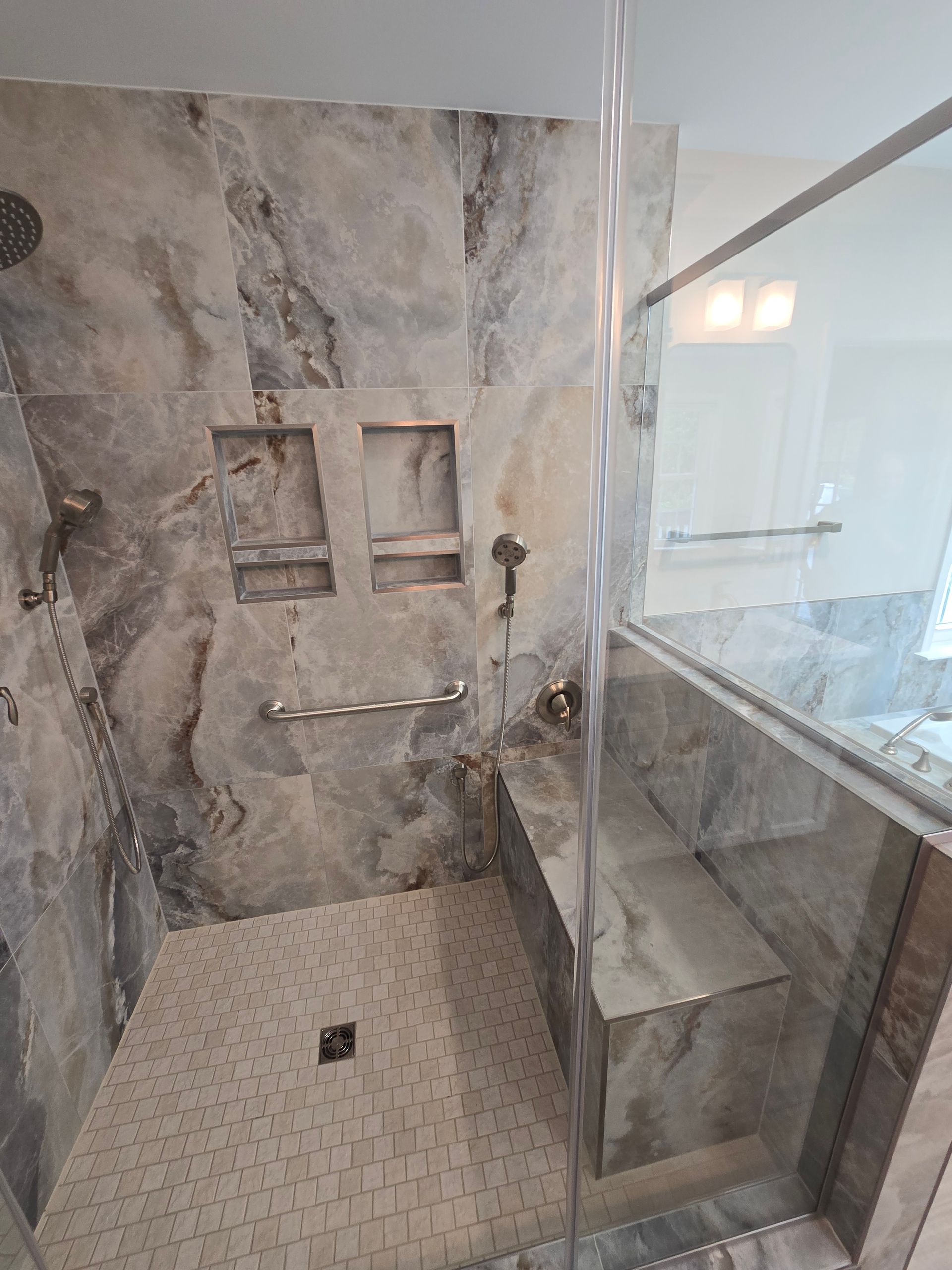 Marble-tiled shower with a built-in bench, two niches, and grab bar.
