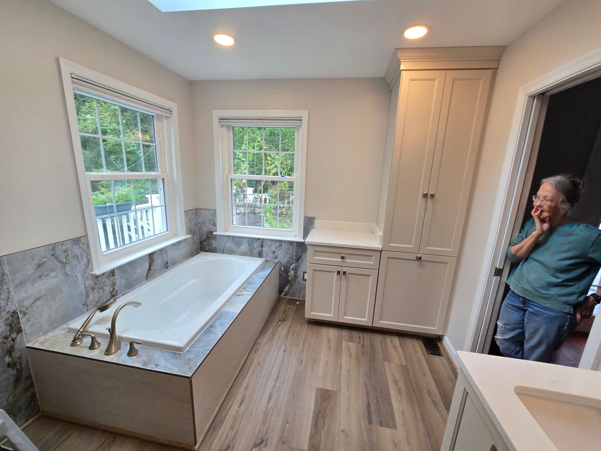 Bathroom remodel with new tub, cabinets, and a woman in the doorway, finished in light neutrals.