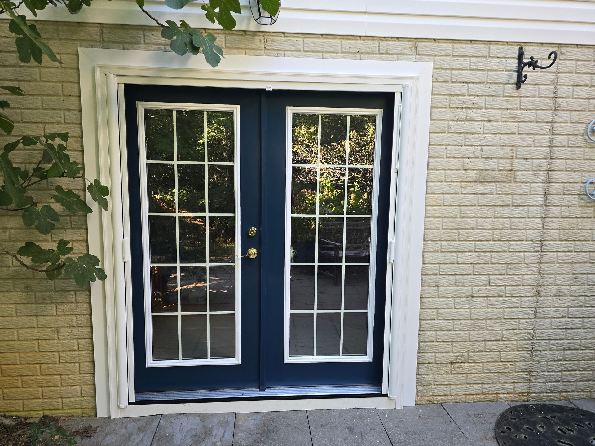 Blue French doors with white grids and trim, set in a brick wall.