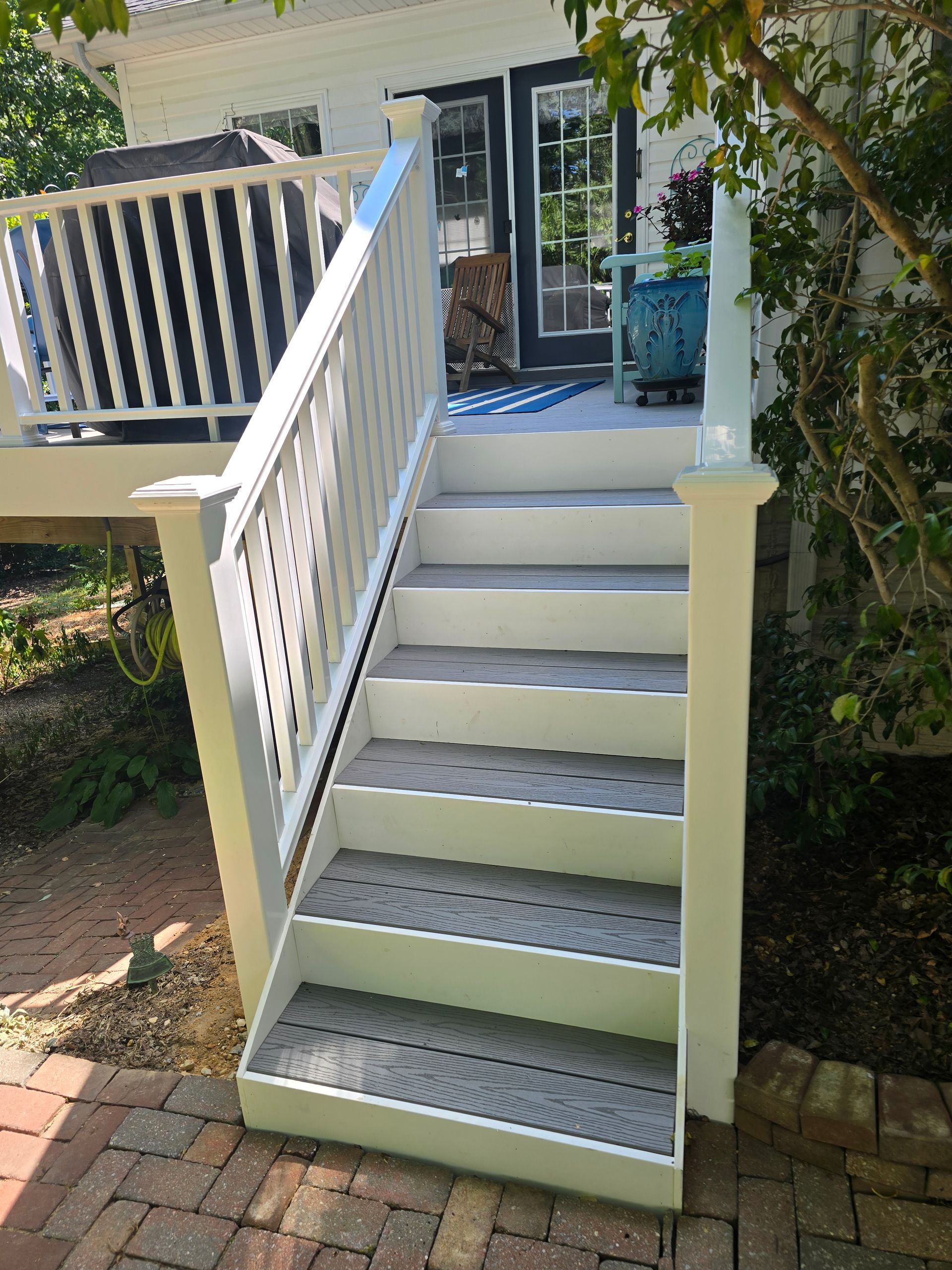White stairs with gray non-slip treads lead to a deck. Brick path surrounds the stairs.
